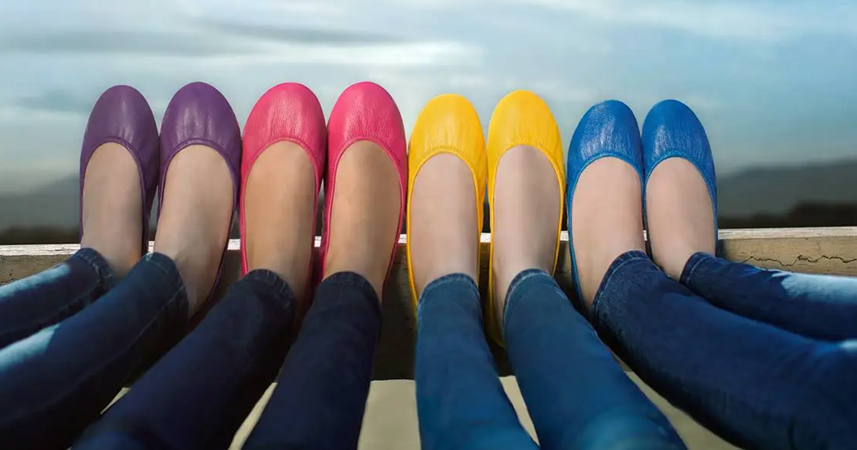 women with feet up on a wooden beam, wearing various colorful tieks shoes with the sky in the background