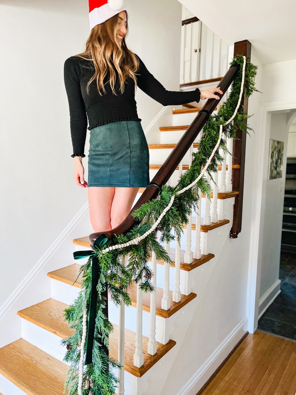 woman standing on staircase holding onto decorated railing with garland