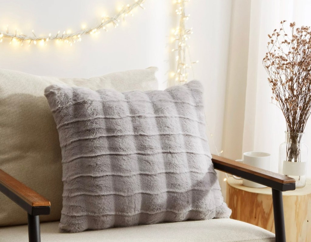 gray faux fur throw pillow on accent chair with holiday lights on wall