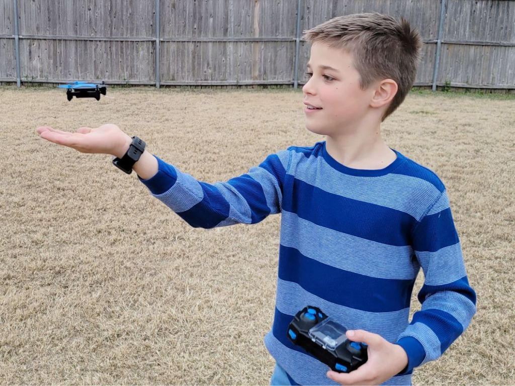 Boy with a remote control in his left hand with a mini drone hovering at eye level over the open palm of his right hand