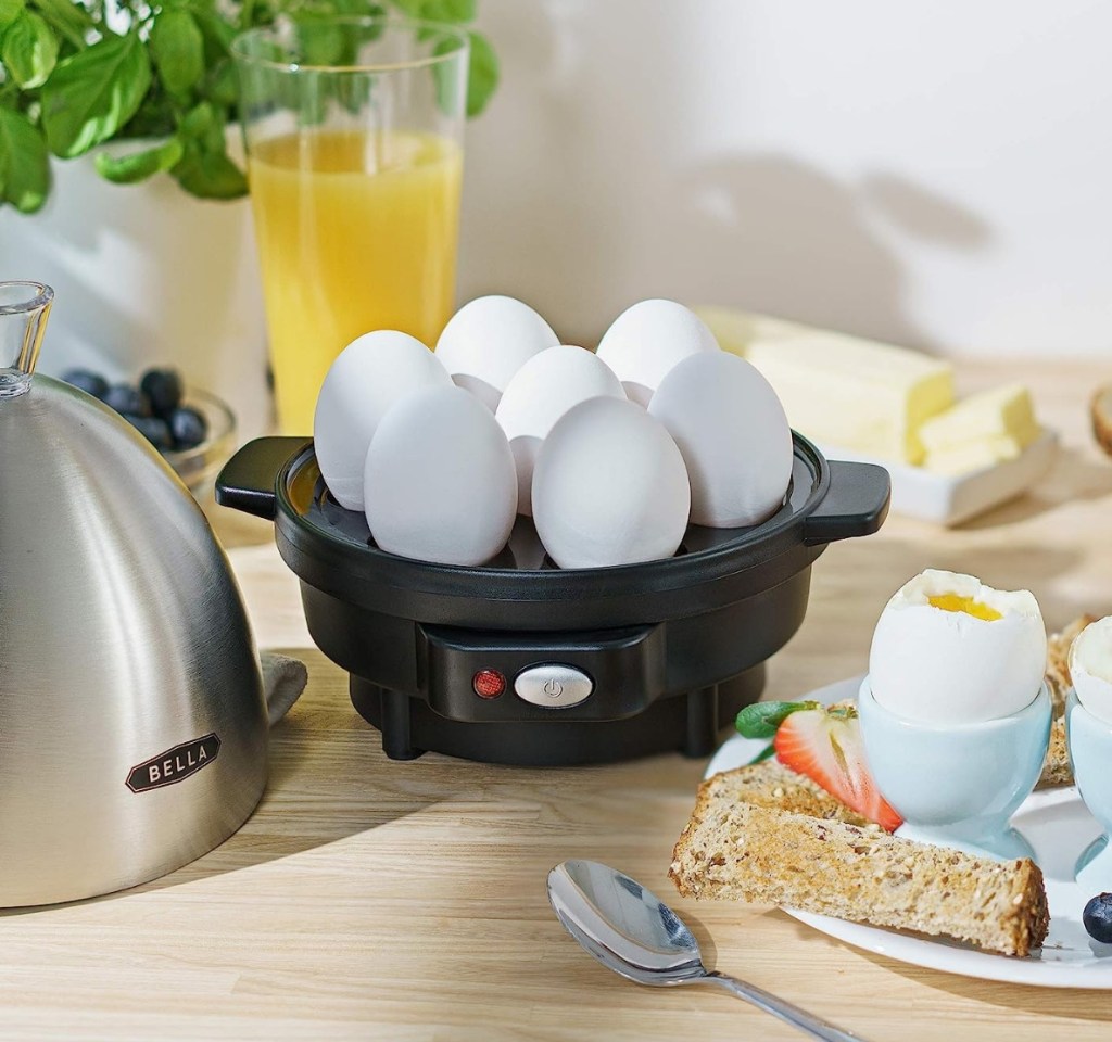 Egg cooker with 7 eggs in it and poached eggs on a plate next to it
