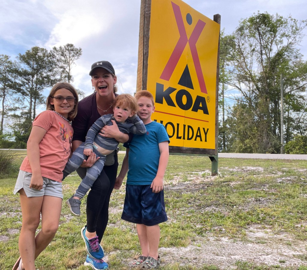 A family posing outside a KOA Holiday Campground Sign 