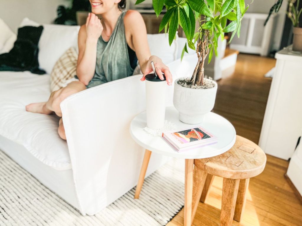 woman sitting on couch next to a Fancyarn Beach Wood Side Table with her hand on a tumbler