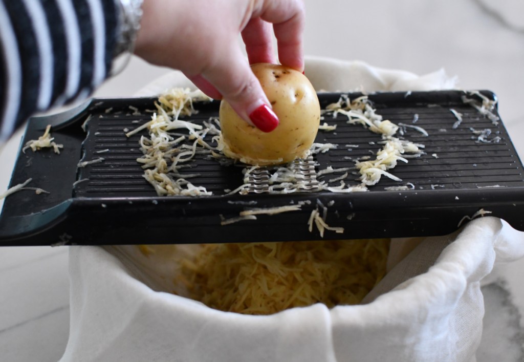 a hand demonstrating how to grate potatoes for latkes, a jewish recipe for hannukah