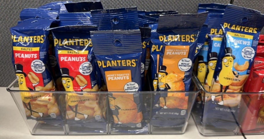 individual packs of different flavors of Planters Peanuts in a plastic bin on a pantry shelf