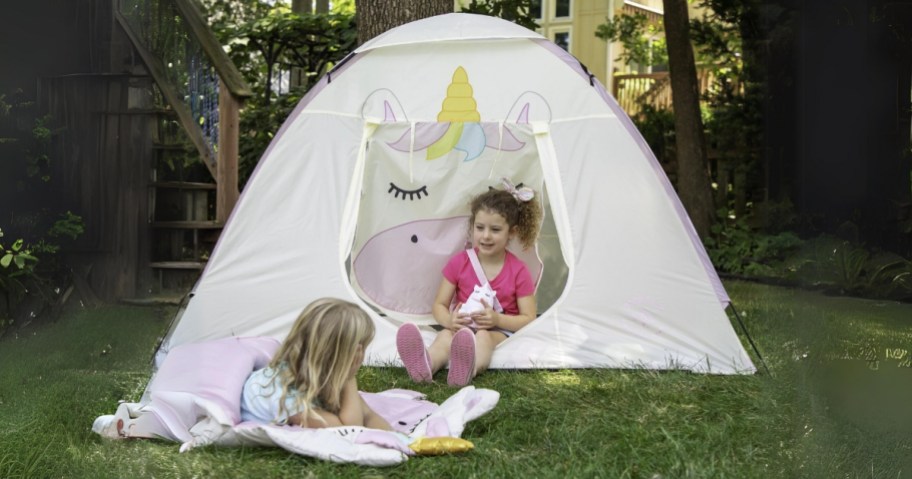 little girl sitting inside the opening of a Unicorn tent, holding a Unicorn lantern, another little girl laying on a unicorn sleeping bag