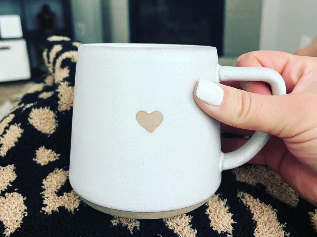holding a white mug with a tan heart on it