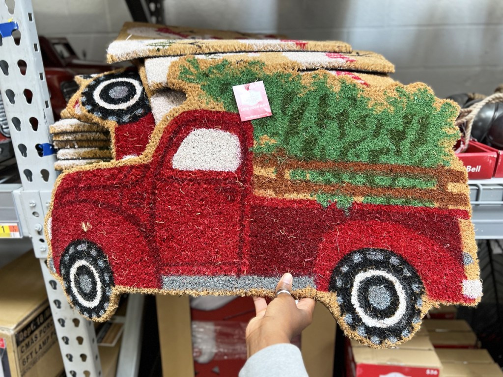 hand holding a doormat of a red truck with a christmas tree in the back