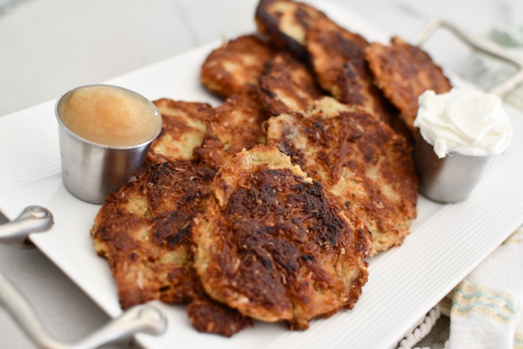several jewish potato latkes displayed on a serving tray with applesauce