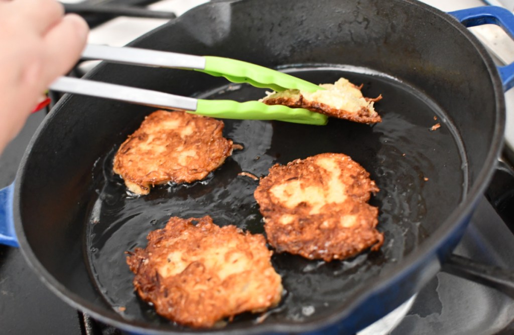 Hand demonstrating how to cook potato latkes in a pan