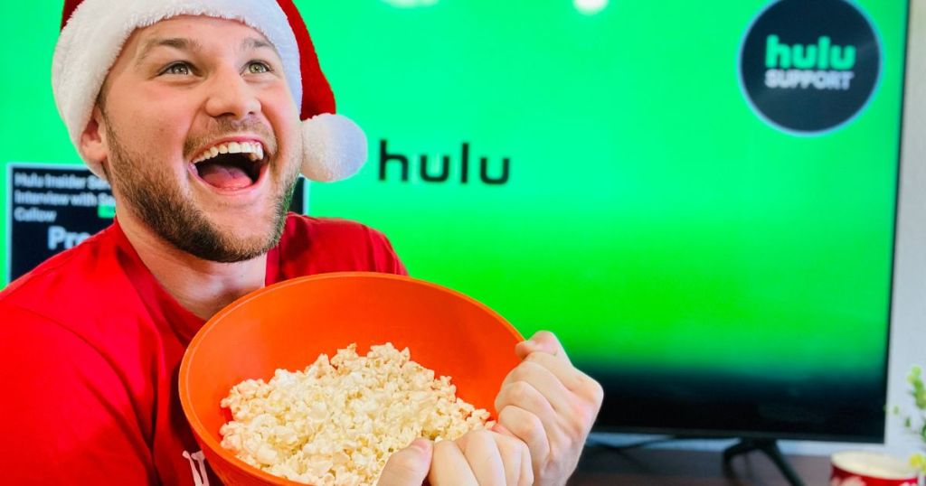 man holding a bowl of popcorn by a TV with hulu on it