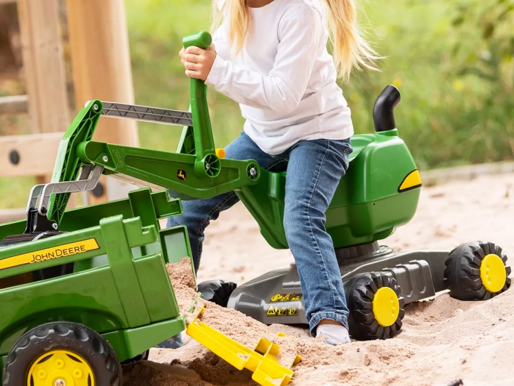 girl playing with a green John Deere Digger ride-on