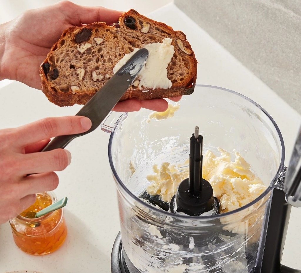 Hand buttering bread with a food processor behind them