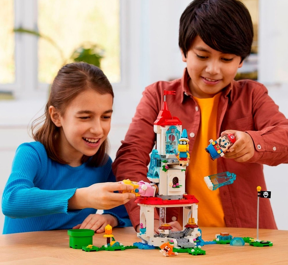 Two kids playing with a LEGO Super Mario set with a LEGO Mario and a LEGO Peach figure