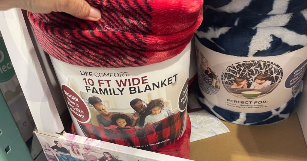 A hand reaching for a red family blanket in a store with a blue one behind it 