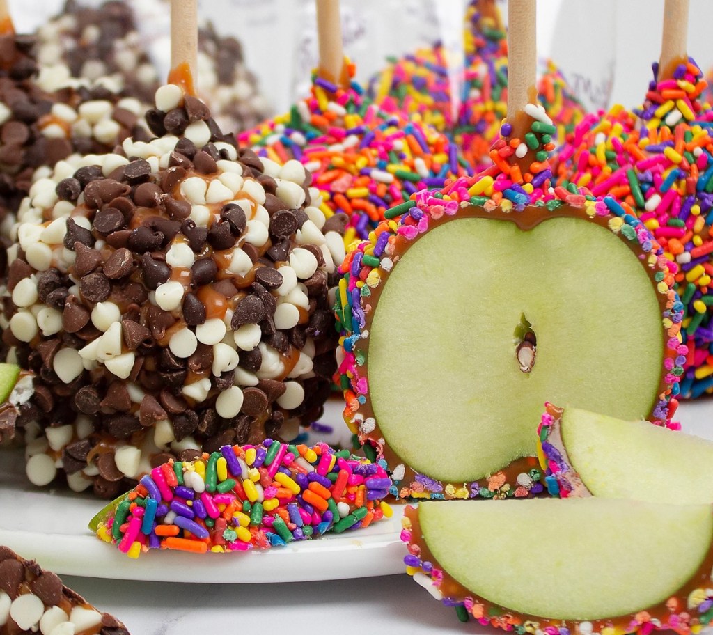 Caramel apples with chocolate and sprinkles on a plate with apple slices in front of them