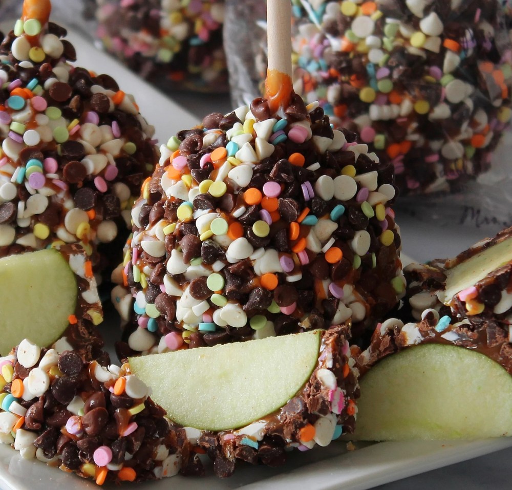 Caramel apple with sprinkles on it and slices of the apple in front of it
