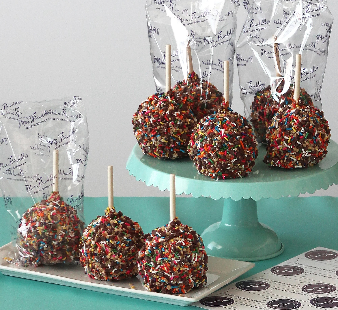 Caramel apples with sprinkles on them on a tray and on a cake stand