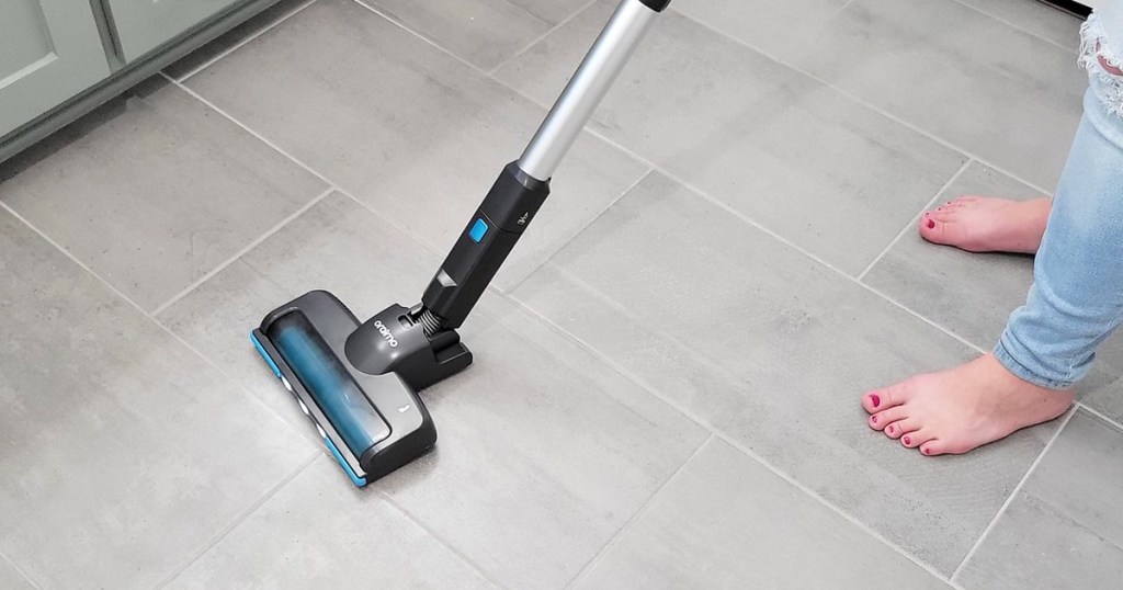 woman using a cordless stick vacuum on tile floor