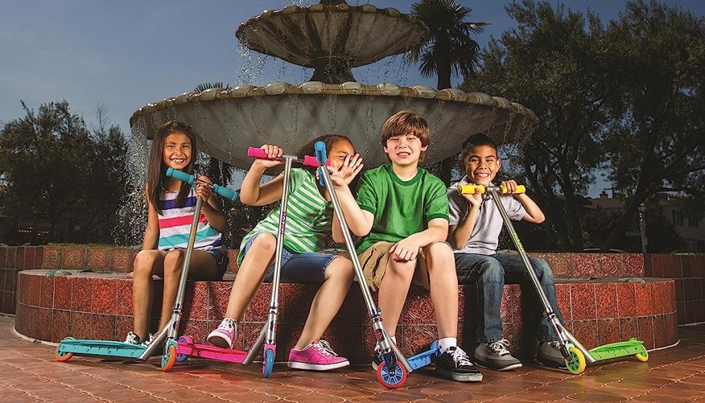 Group of kids sitting by a large water fountain and holding Razor scooters