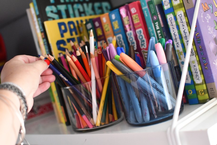 hand grabbing a colored pencil from a container made from a candle jar