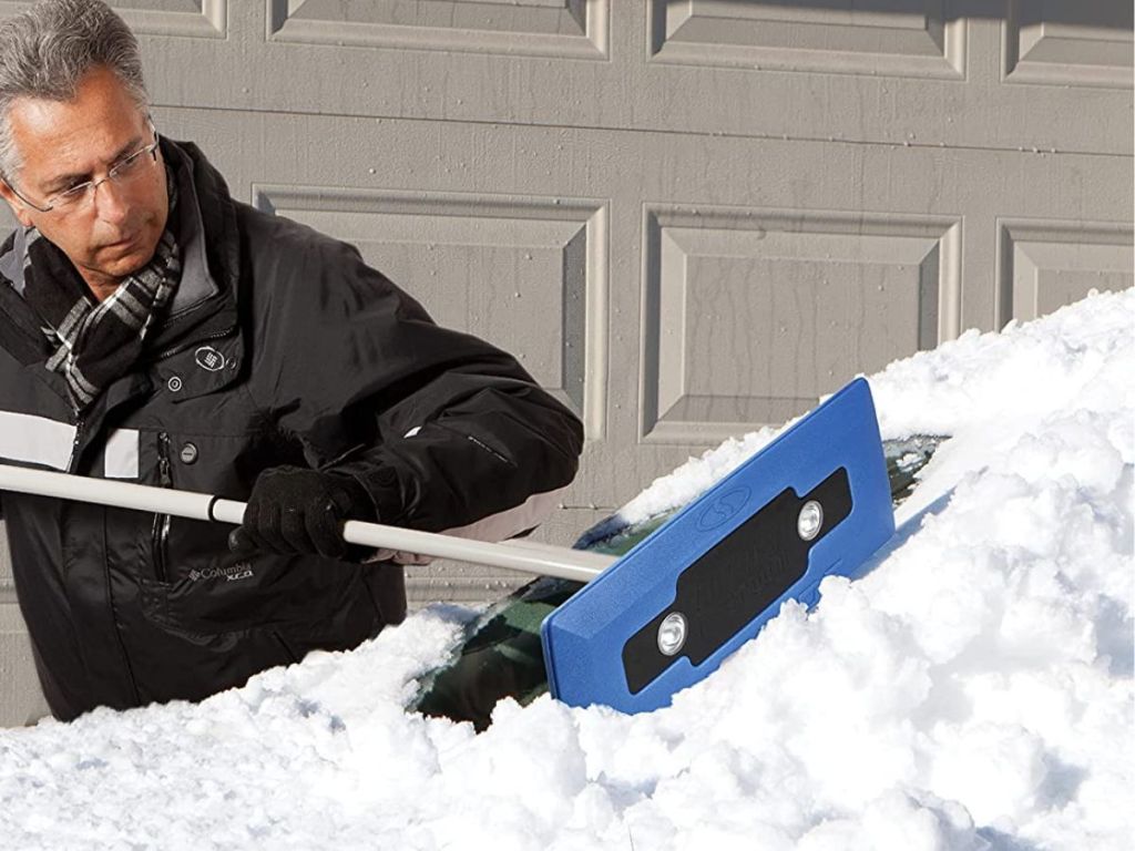 Man cleaning snow off a windshield using a snow broom