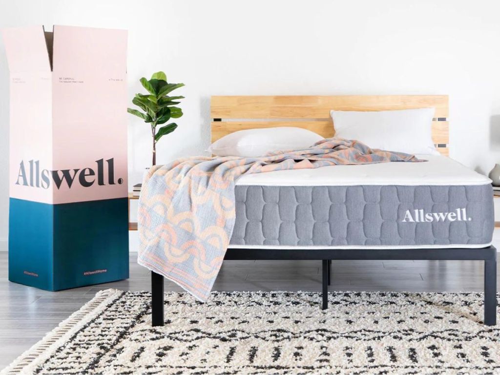 Allswell mattress with pink and gray blanket and pillow on mattress in bedroom with opened Allswell box beside bed