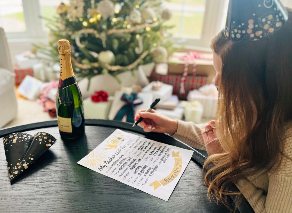 Woman in a party hat filling out her New Year Bucket List at a table next to her champagne