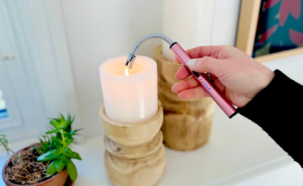 hand holding rose gold bendable electric lighter over pillar candles