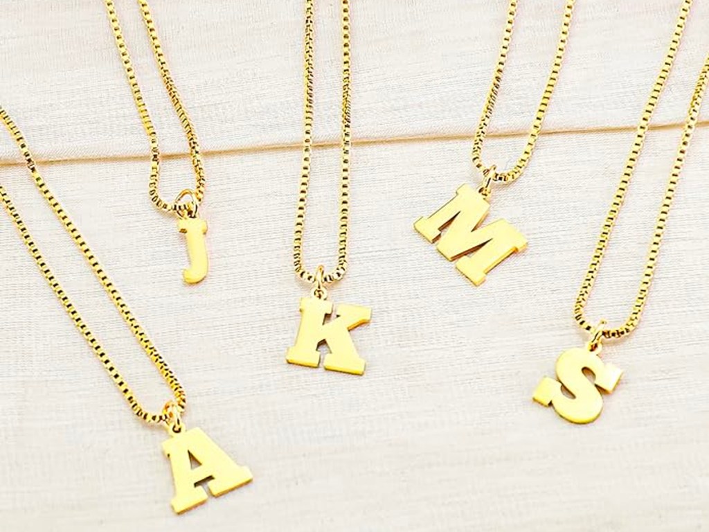 A, J, K, M, and S gold initial necklaces sitting on table