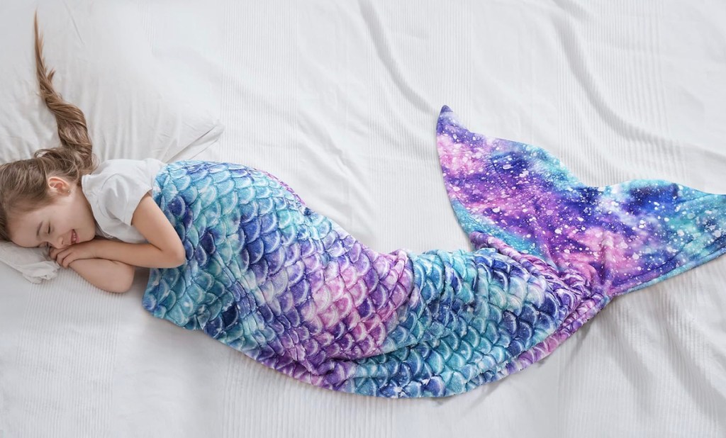 girl laying on white sheet with colorful mermaid tail