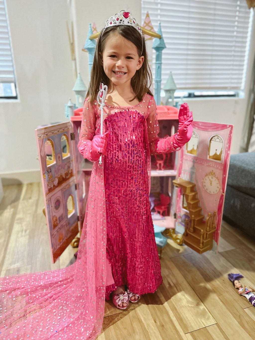 girl wearing pink princess dress in front of dollhouse