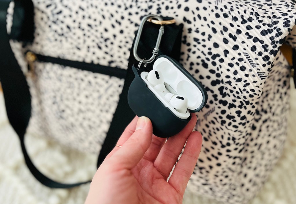 hand holding airpods in black silicone case on leopard duffle bag