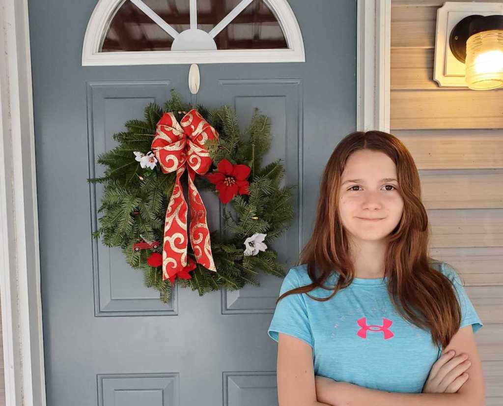 girl standing next to christmas wreath on front door