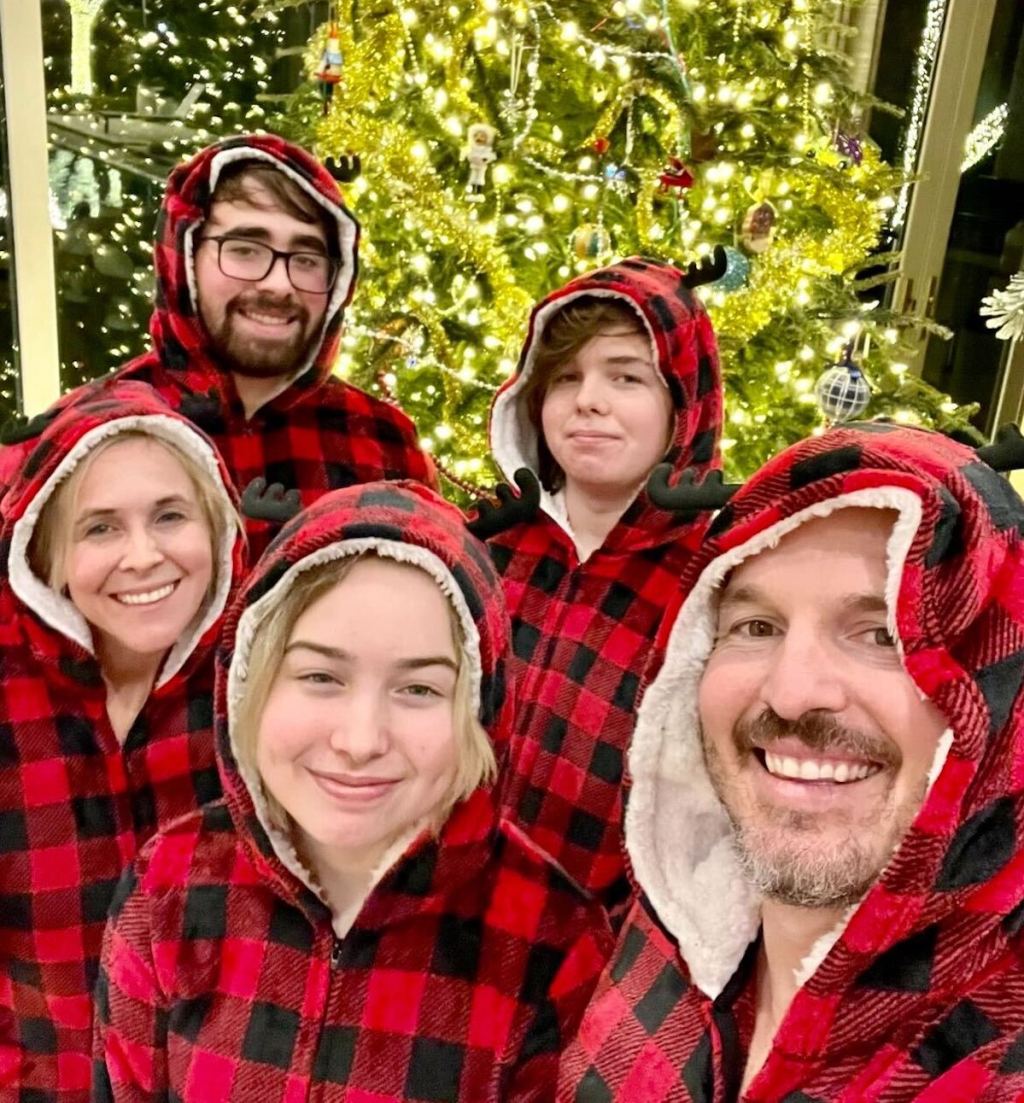 family wearing black and red plaid matching christmas pajamas in front of lit christmas tree