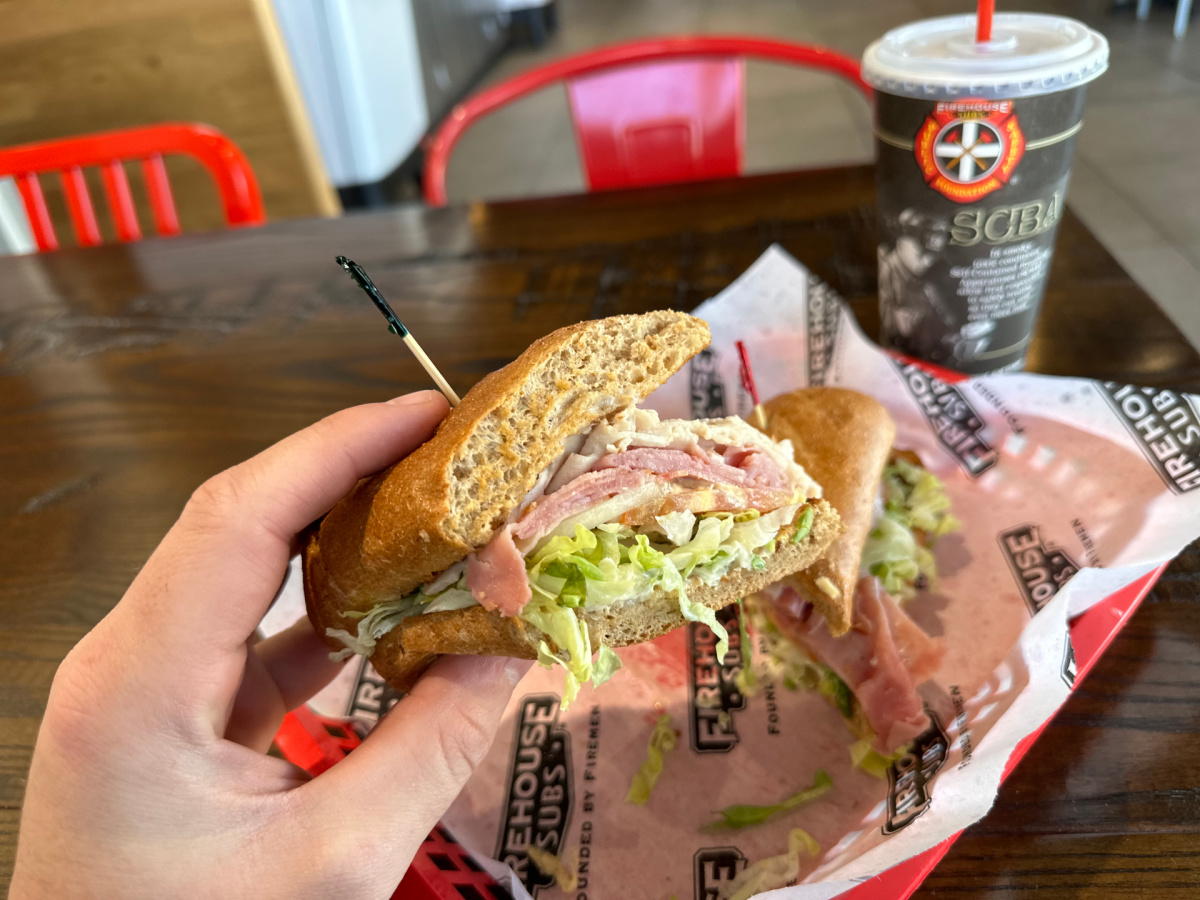 hand holding half a firehouse sub, one of the birthday freebies of 2024, above a basket and drink cup