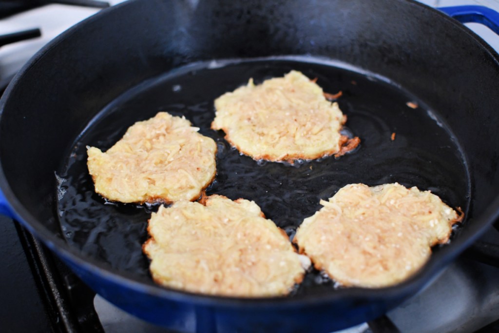 frying four latkes in a cast iron pan