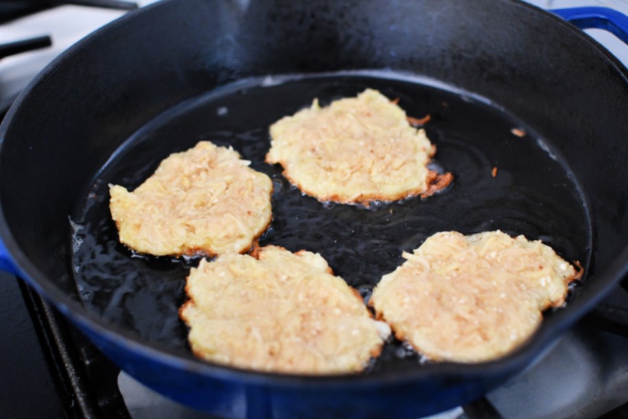 frying four latkes in a cast iron pan
