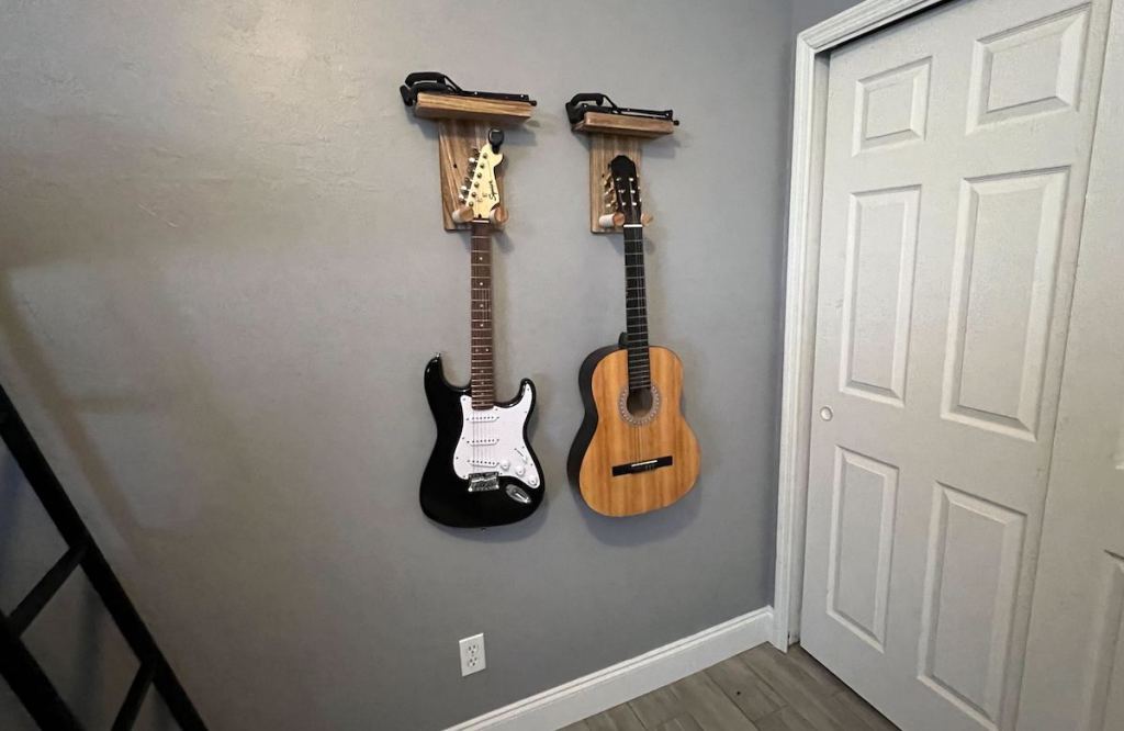 two guitars hanging from wall mounted hangers on gray wall