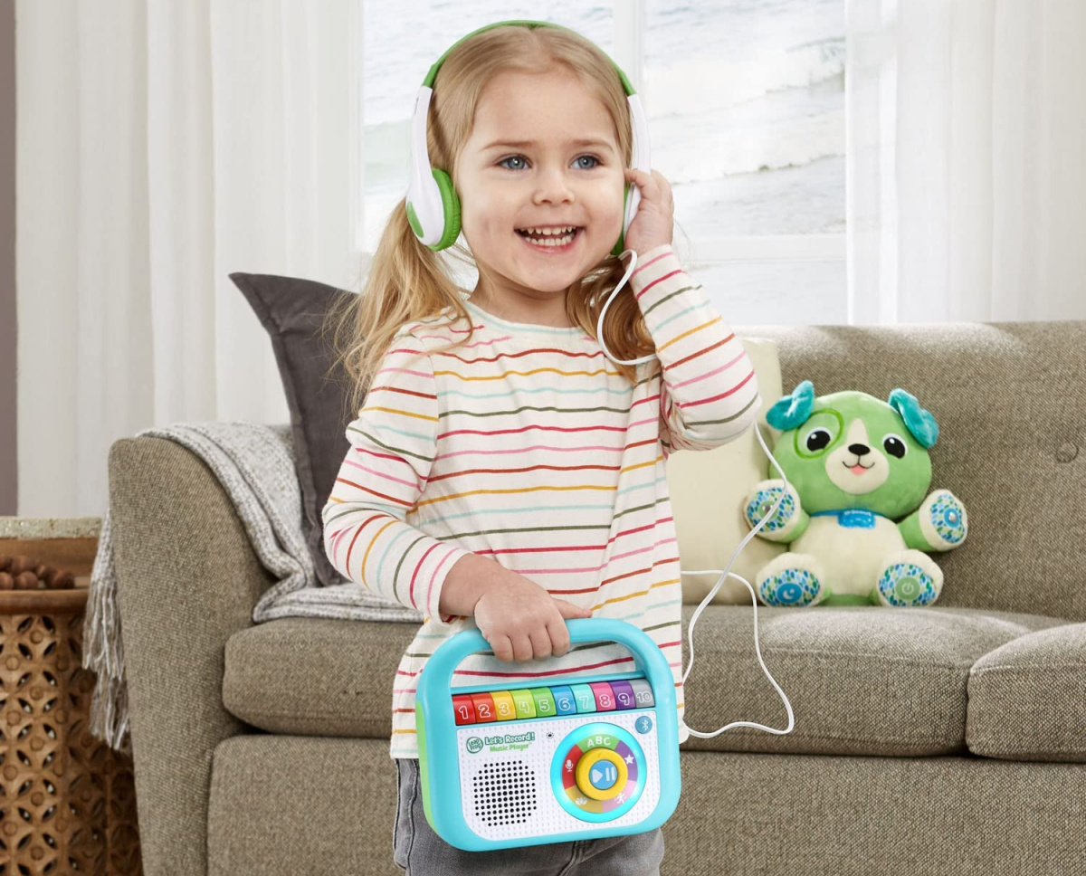 smiling girl playing with a leapfrog music player while wearing headphones