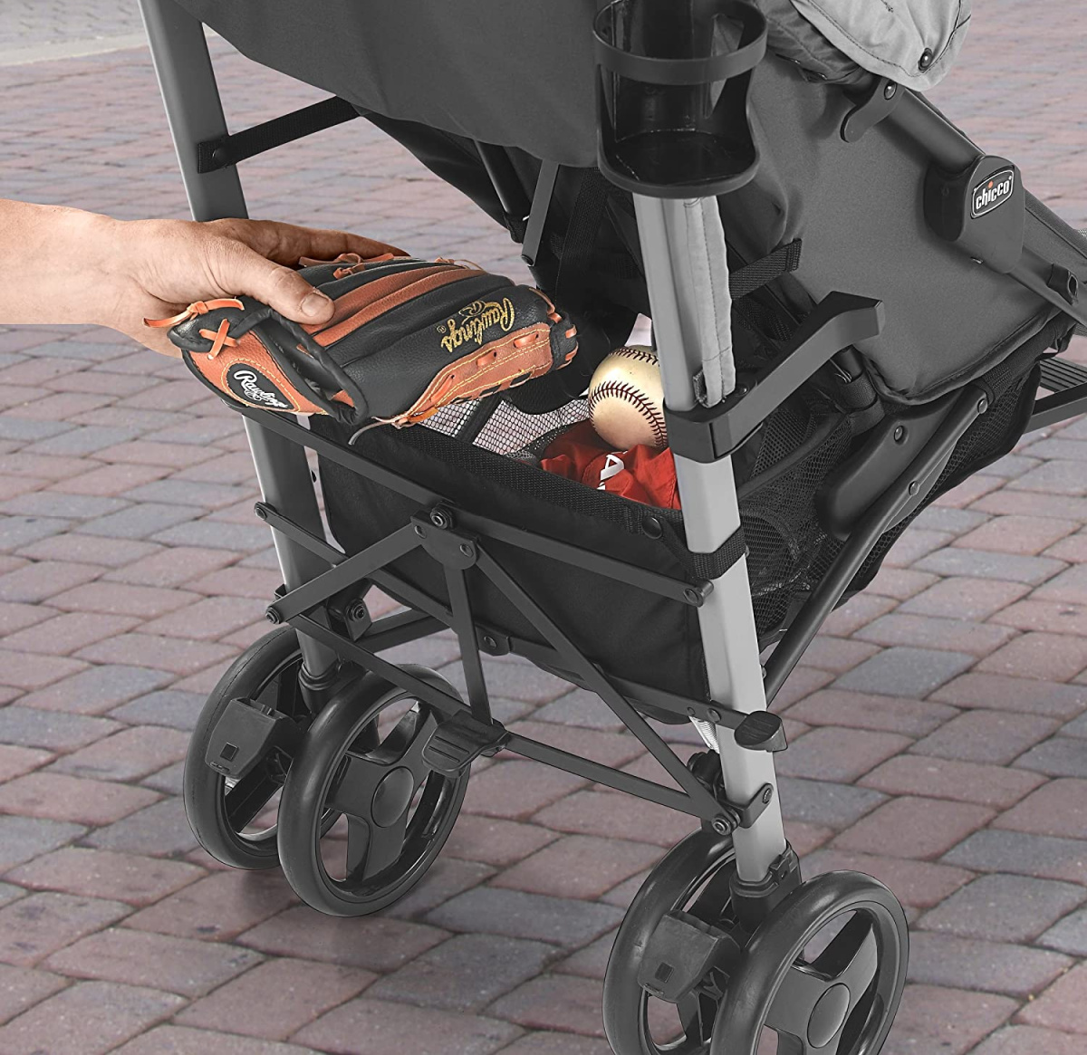 hand loading a liteway chicco stroller basket with a baseball glove and other sports accessories