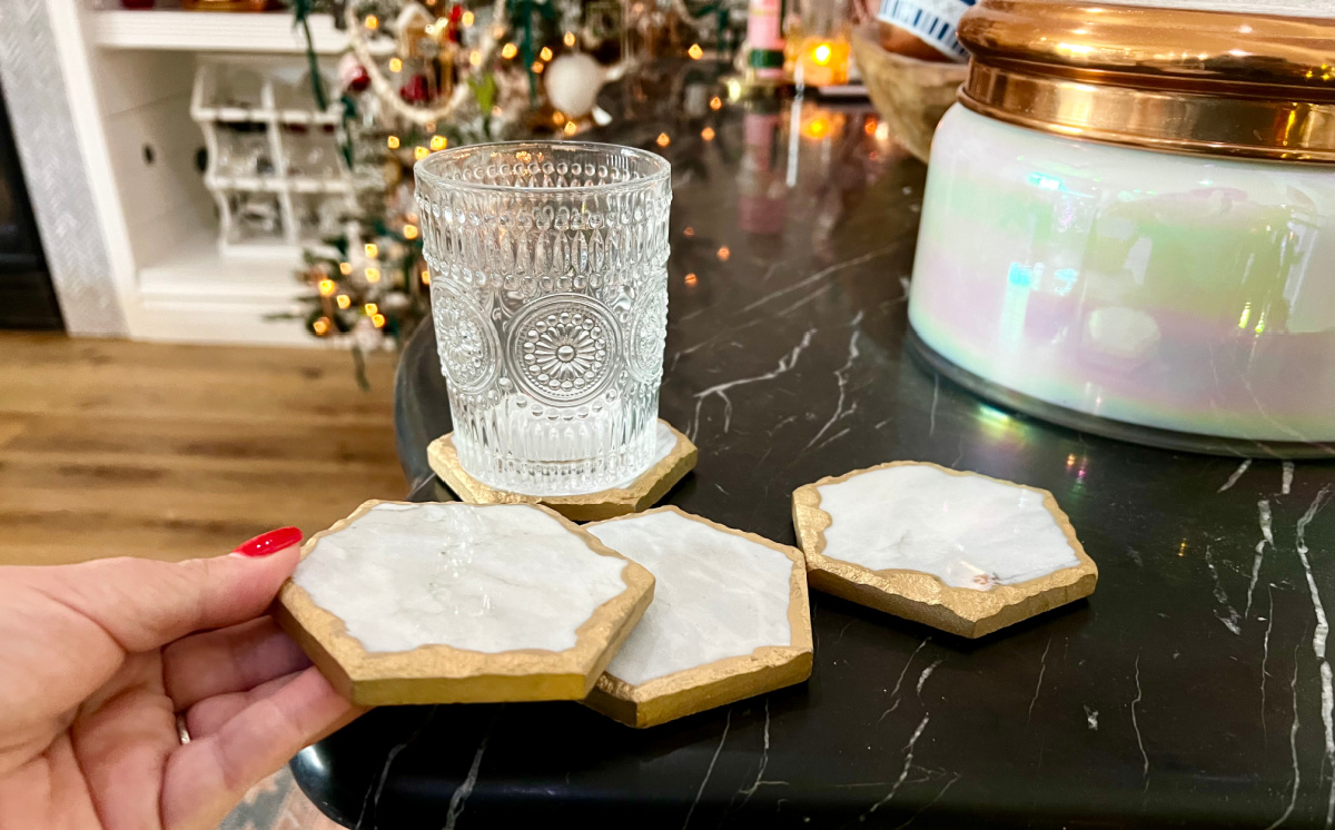 hand touching the edge of a marble coaster sitting near a large capri candle