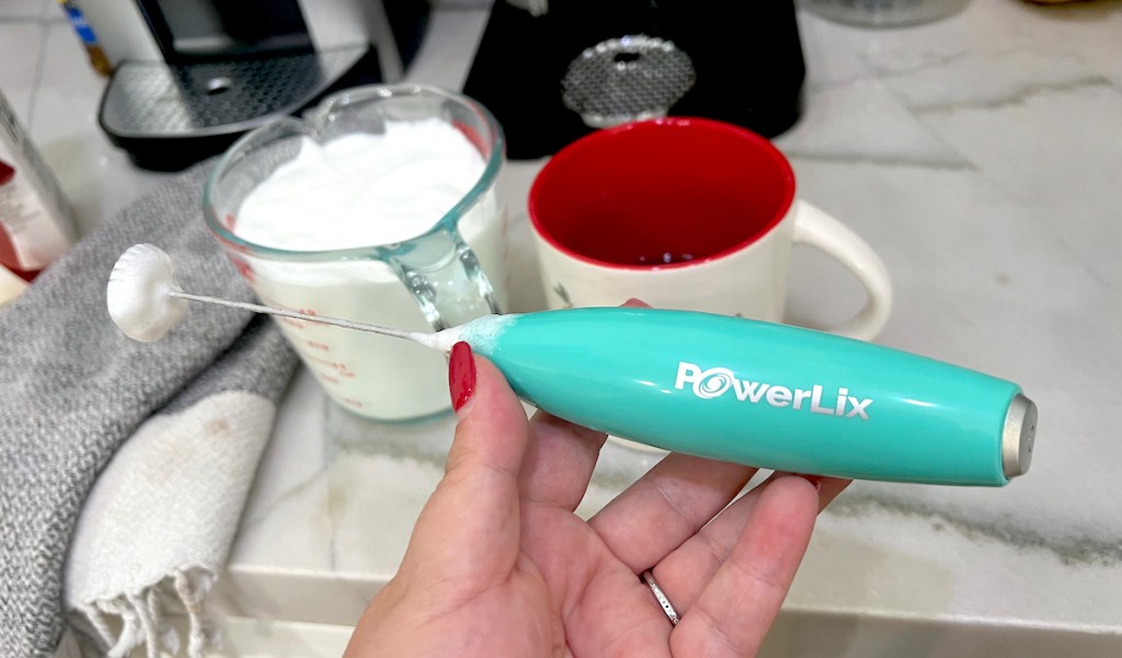 hand holding a teal powerlix milk frother over kitchen counter