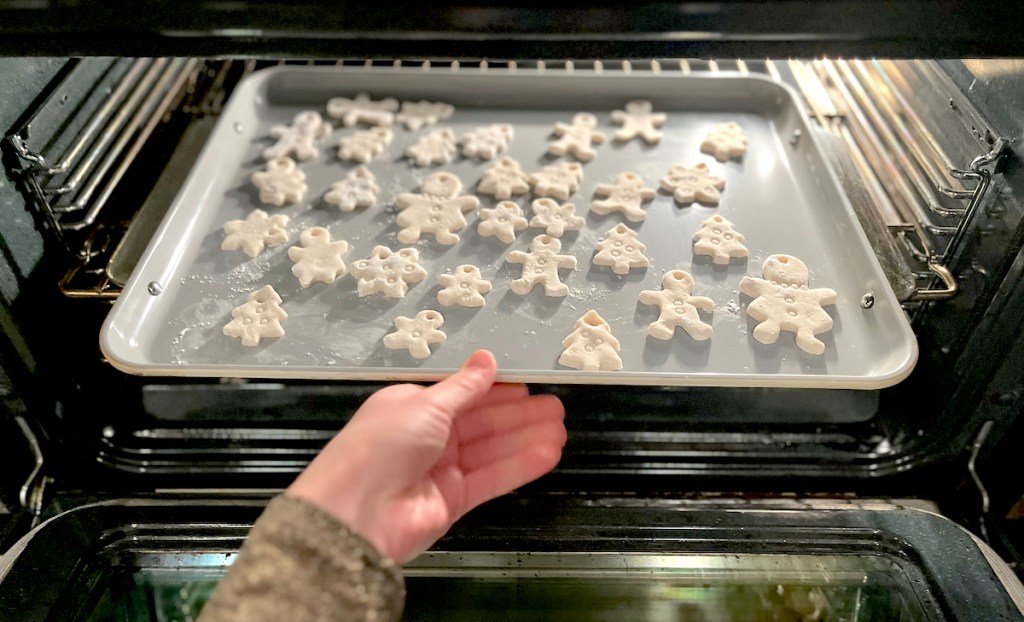 hand putting baking sheet in oven with cut out shapes