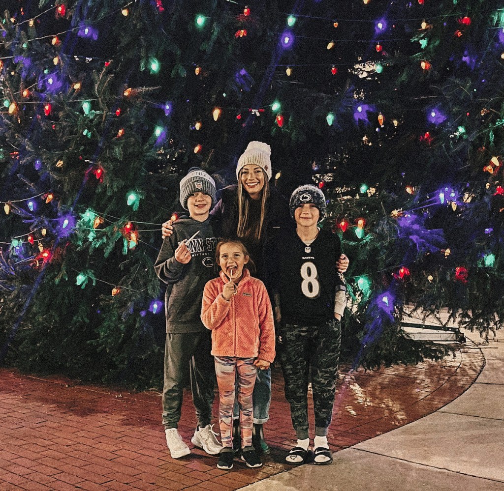 family standing outside in front of large colorful lit tree