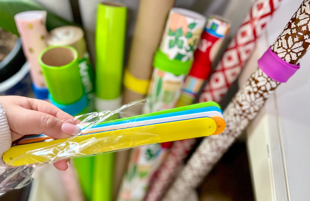 hand holding stack of slap bracelets in front of wrapping paper rolls