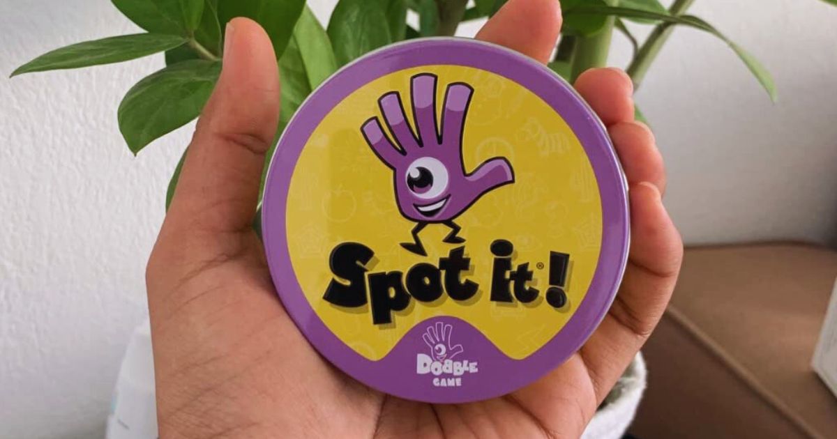 يد تمسك بـ Spot It!  لعبة القصدير