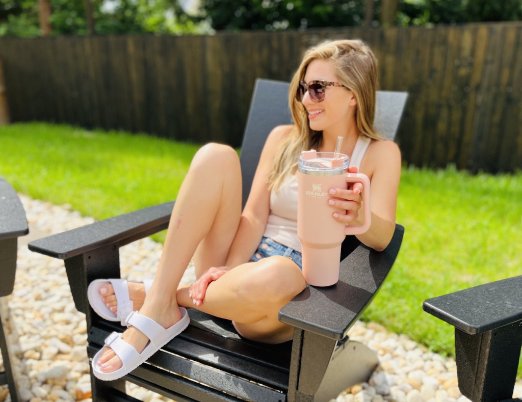 woman sitting on black outdoor chair holding pink stanley mug