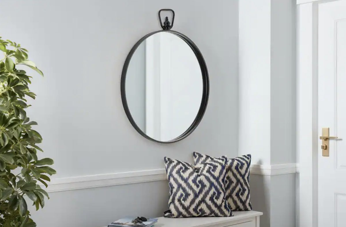 black framed round mirror hanging on wall above entry bench with pillows