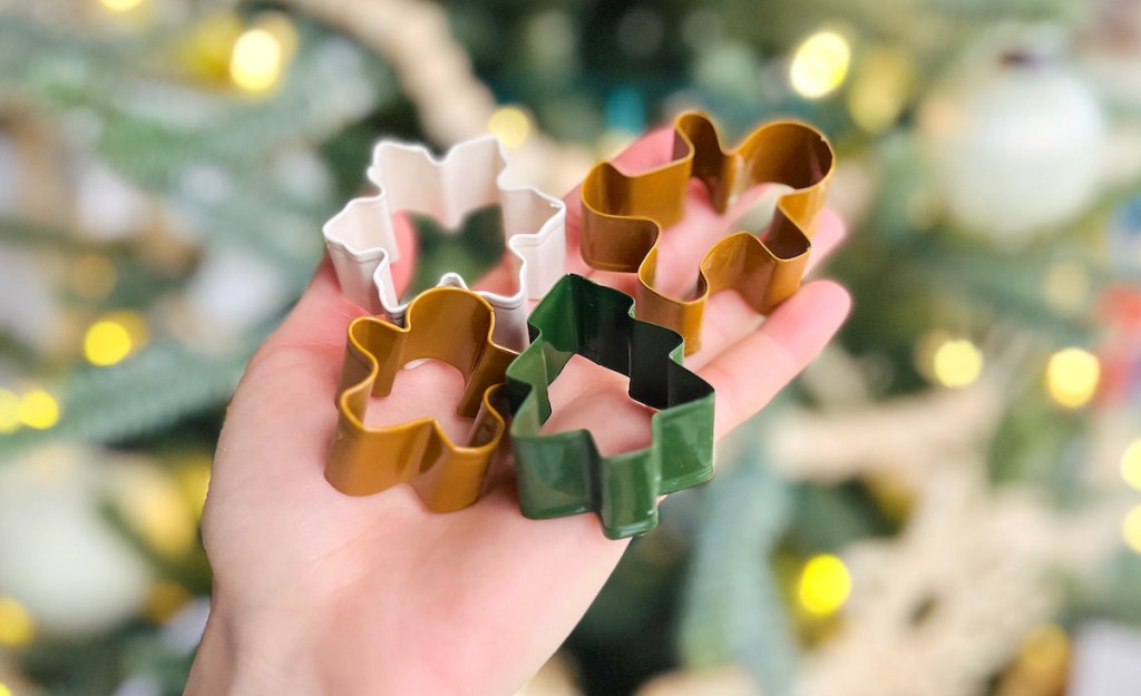 hand holding various cookie cutters in front of lit tree